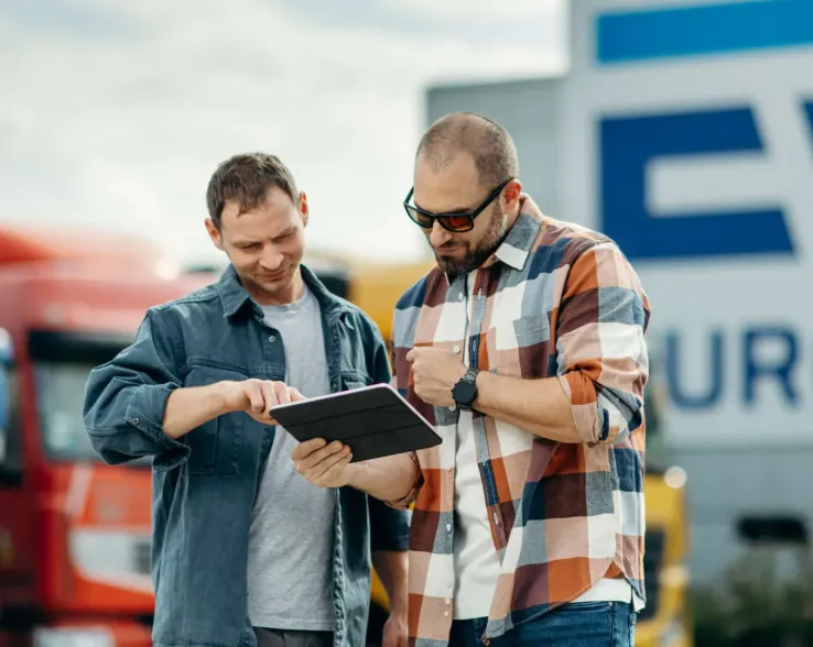 Two man reading from a  tablet standing in front of Eurowag sign